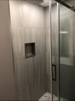 bathroom shower with large marble tiles, recessed soap holder, and glass doors